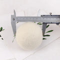 A natural wool drying ball for tumble dryers next to a plain cotton storage bag on a laundry background.