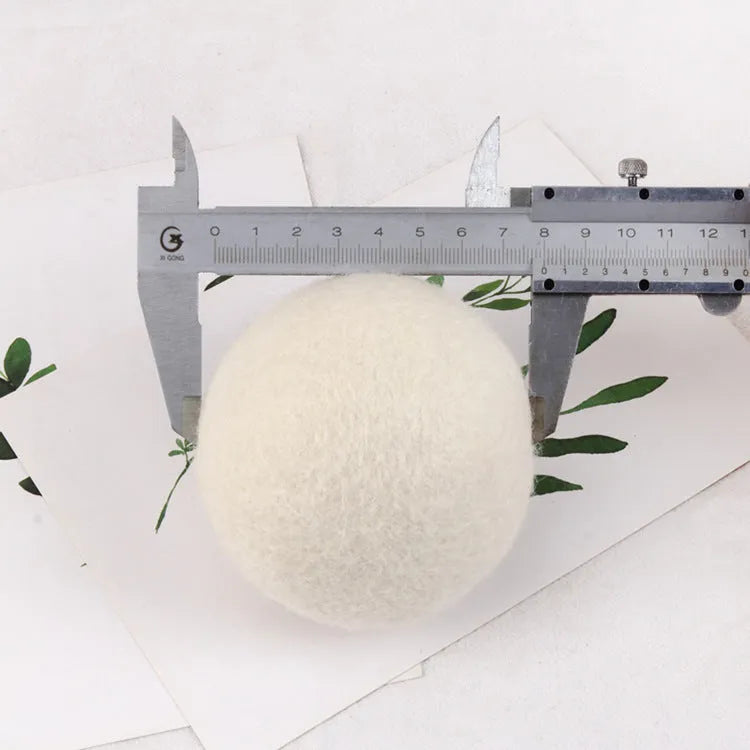 A natural wool drying ball for tumble dryers next to a plain cotton storage bag on a laundry background.