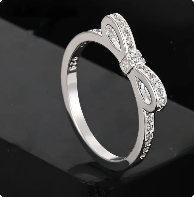 Silver bow-shaped ring with sparkling rhinestones and zircon crystals on a finger.