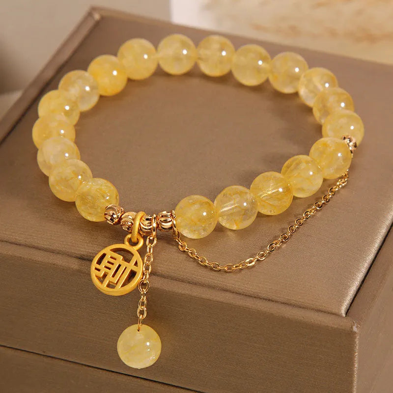 Women's natural citrine bracelet with a gold-tone Chinese character charm and tassel on an adjustable chain.