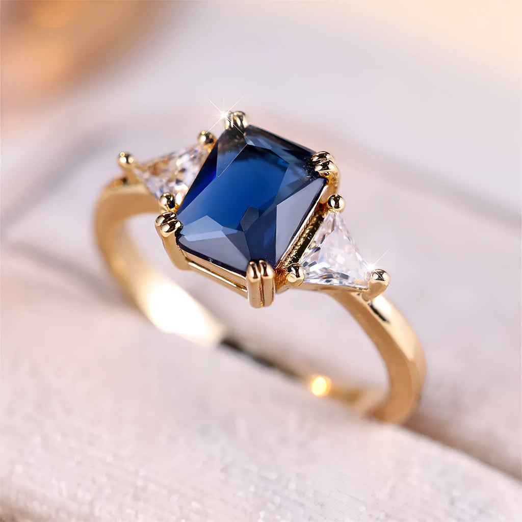 A rectangular gold sapphire blue plated copper ring for women on a plain background.