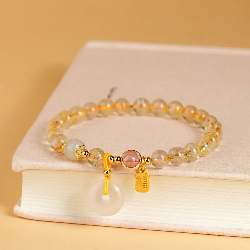Gold rutilated quartz bracelet with geometric safety buckle and pendant on a white background.