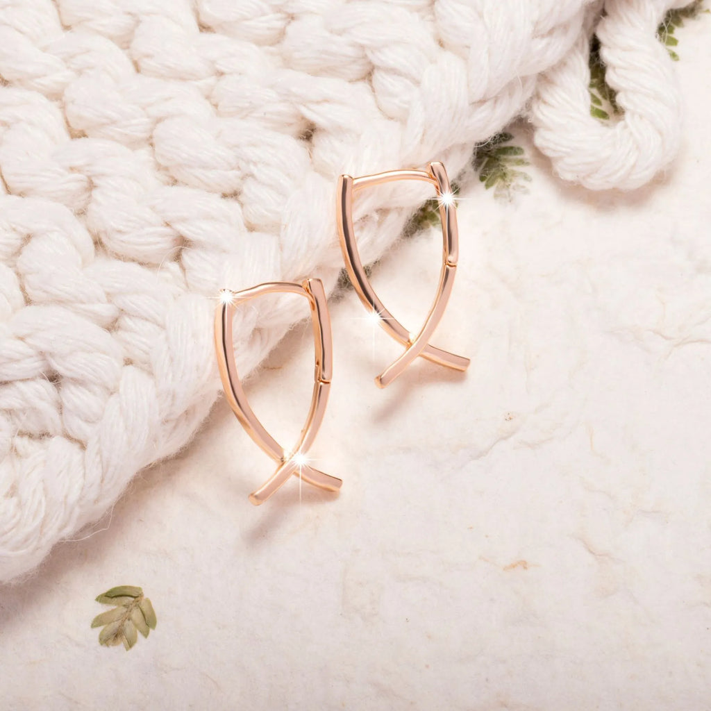 A pair of rose gold coloured cross-shaped earrings made from copper on a plain background.