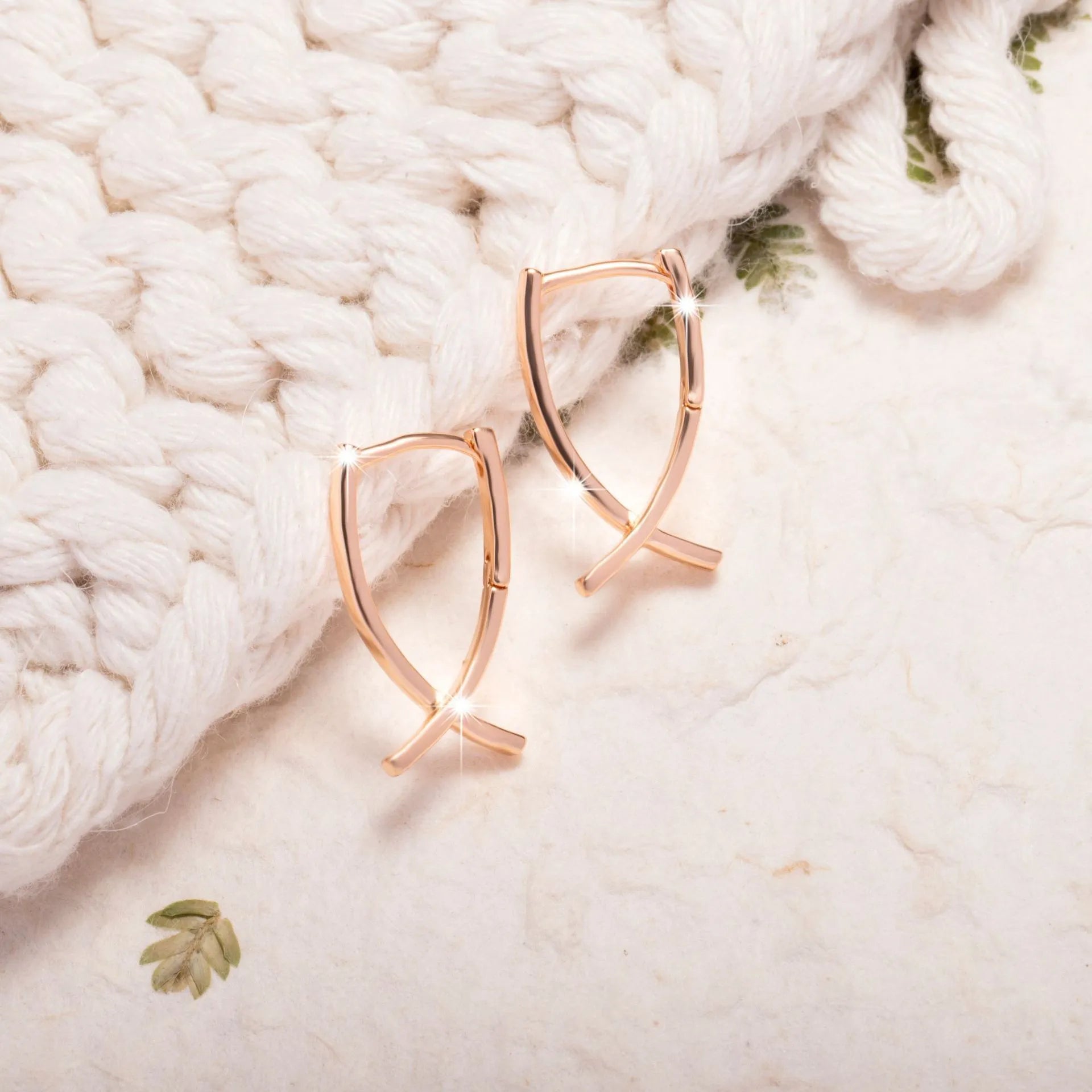 A pair of rose gold coloured cross-shaped earrings made from copper on a plain background.