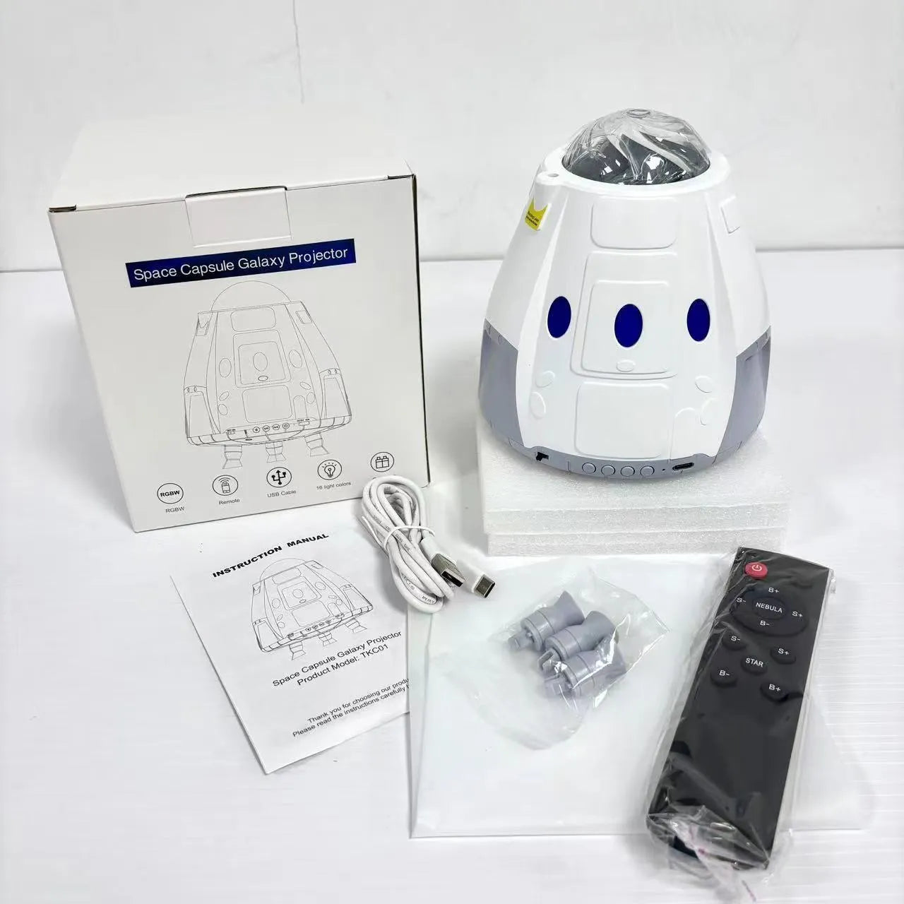 Tall white space capsule galaxy projection lamp with USB cable and remote control on a table.