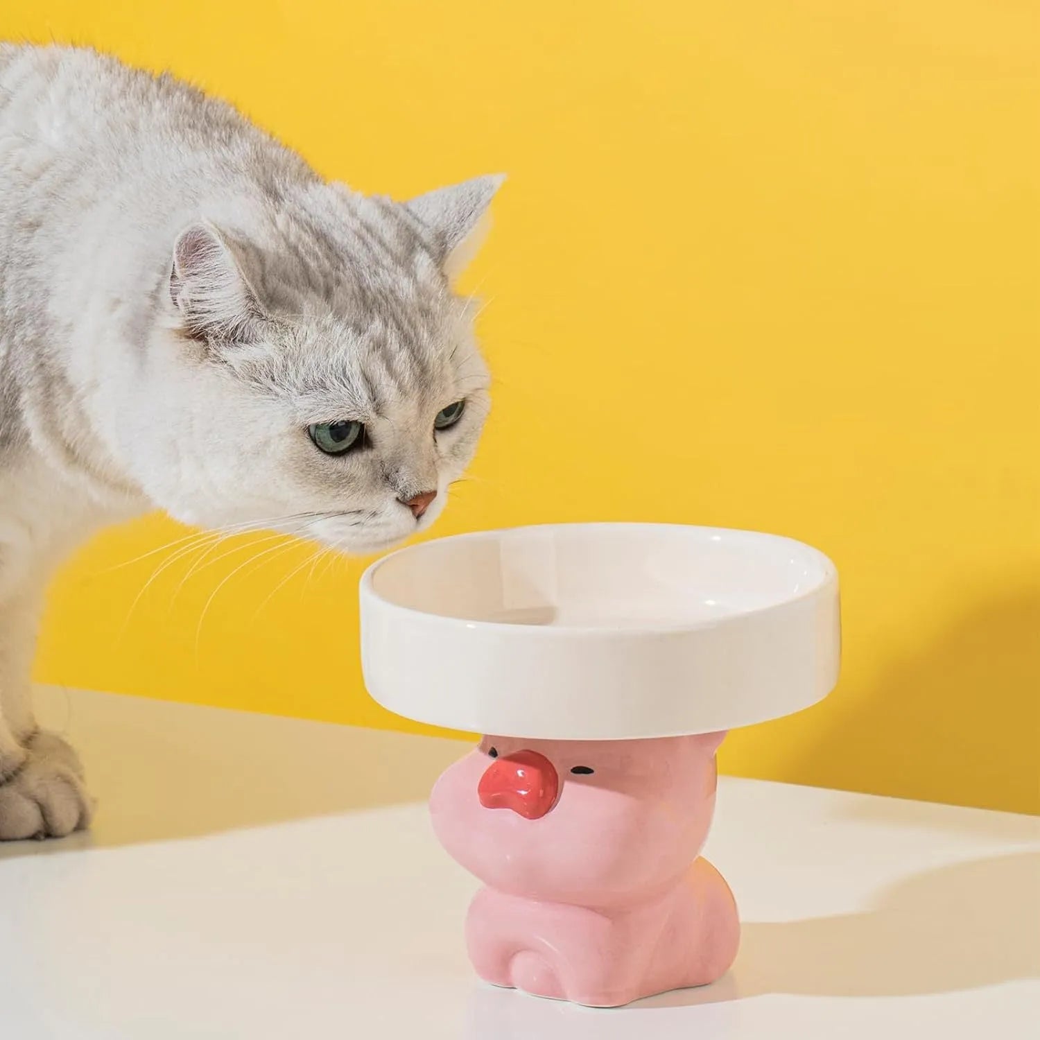 White ceramic raised cat bowl with a bear design, showing its elevated stand and wide feeding dish.