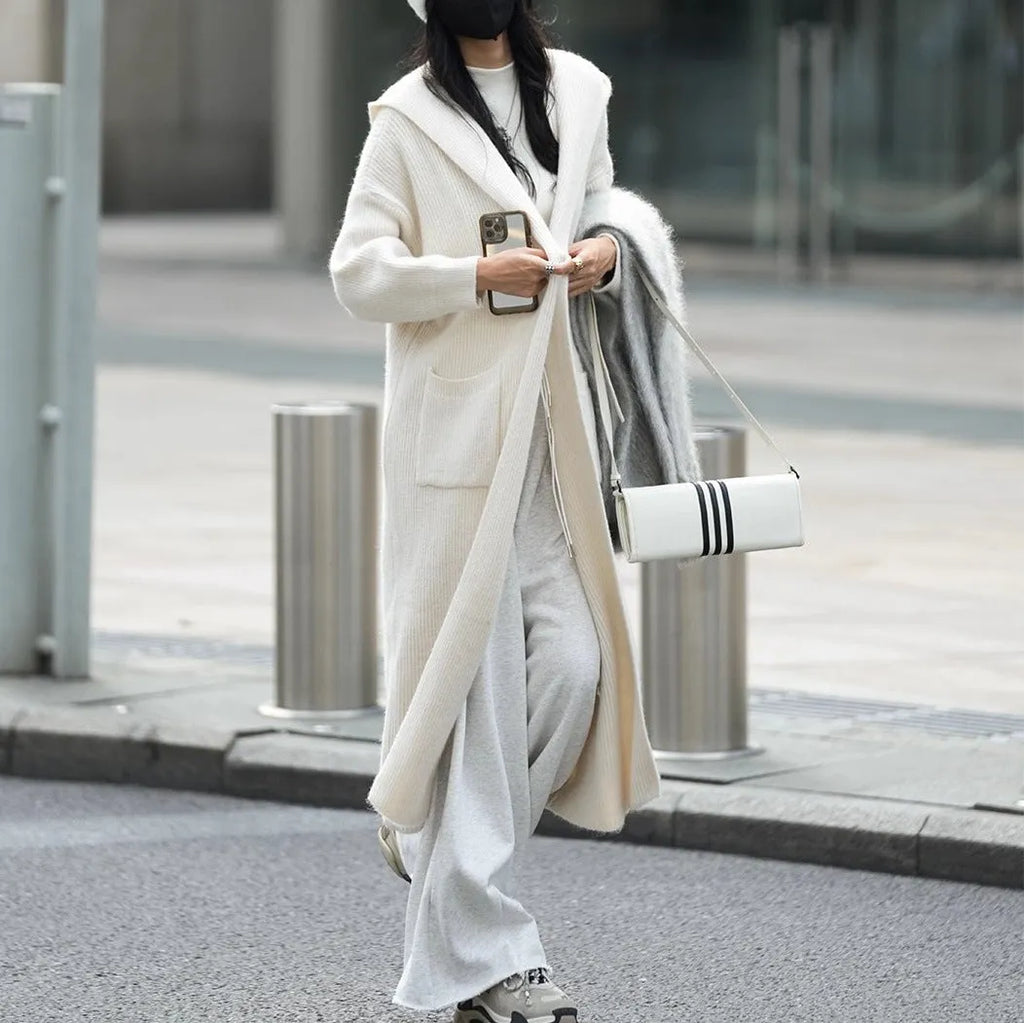 Long grey knitted women's cardigan with a hood, styled like a loose-fit trench coat.