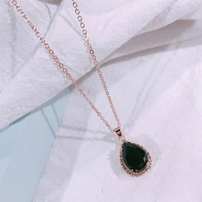 Close-up of a women's rose gold tone drop pendant necklace with pink rhinestone inlay on a model.