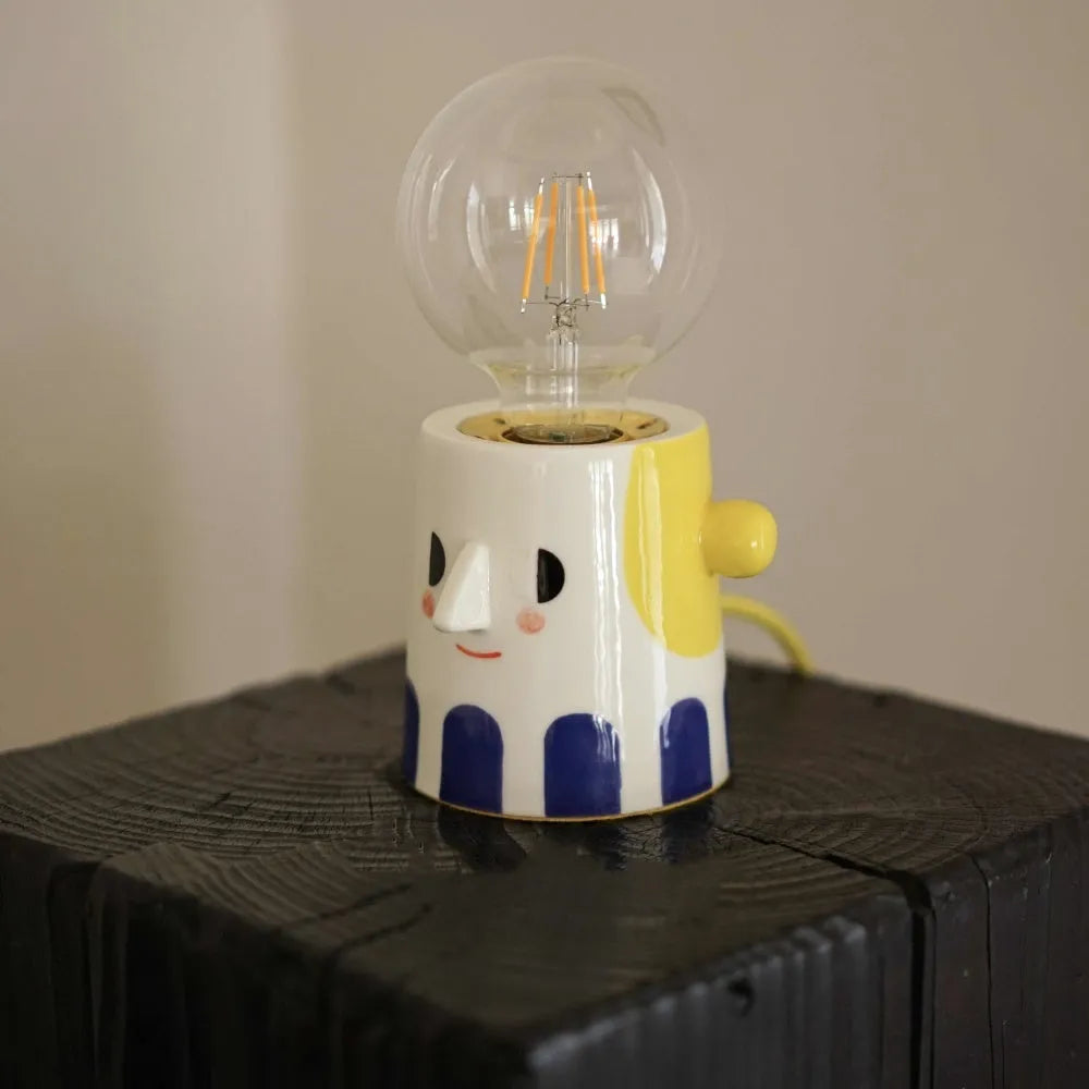 Handmade ceramic bedside lamp with a ball headlight design on a nightstand.