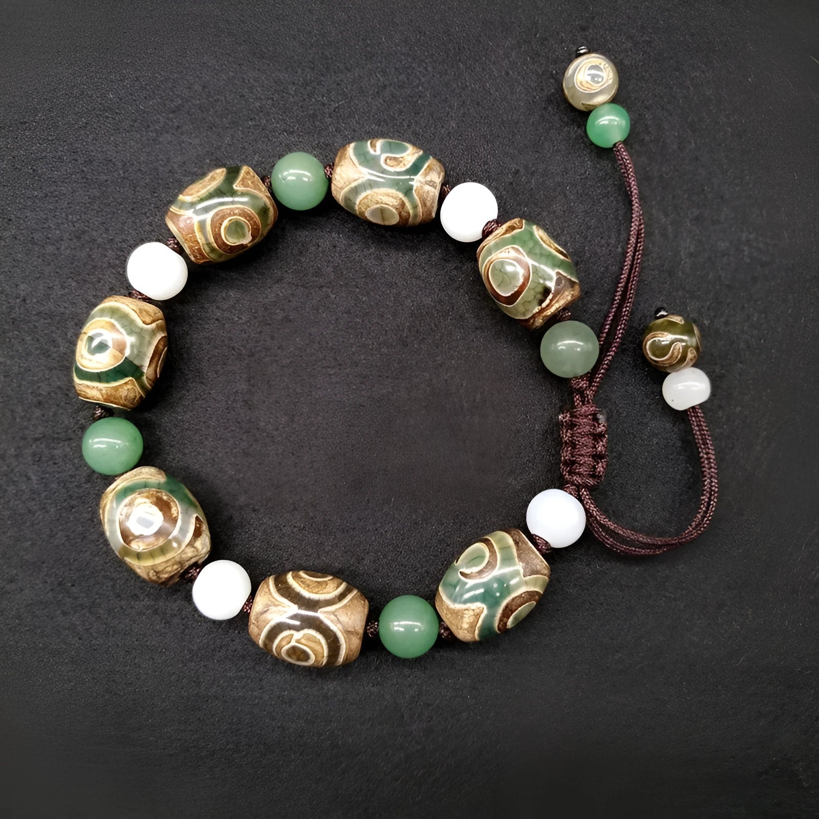Green agate hand-woven Tibetan bracelet with three-eye geometric design on a wrist.