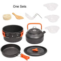 Orange camping cookware set with aluminium pots, pan, and utensils in a mesh bag