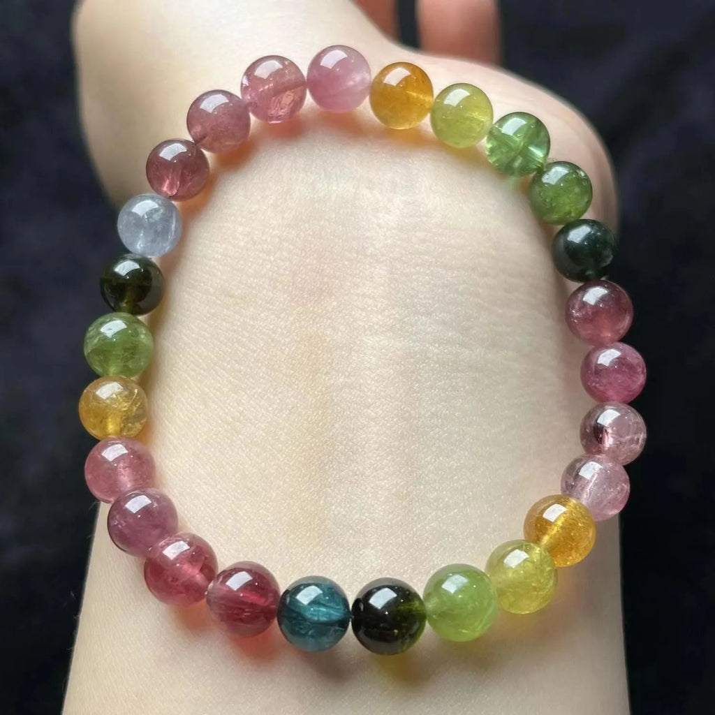 Close-up of a women's silver-toned bracelet with a four-leaf clover charm, pearl pendant, and colourful tourmaline stones.
