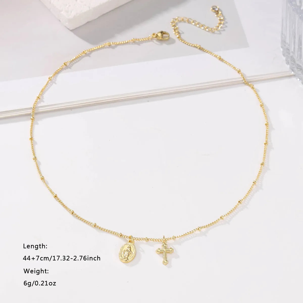 Gold geometric cross Virgin Mary pendant necklace on a chain.