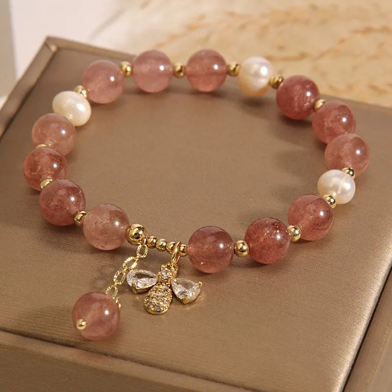 Women's bracelet with strawberry quartz pearls, a zircon bee charm, and alloy links on a wrist.