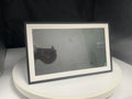 White 15.6 inch smart digital photo frame on a table showing a family photo, with mobile app upload icon.