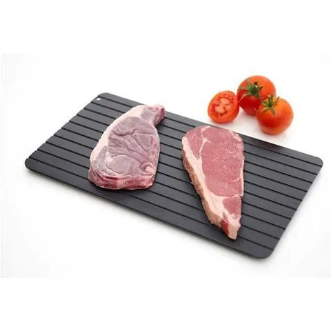 Black aluminium quick defrosting tray for thawing meat and frozen food on a kitchen counter.