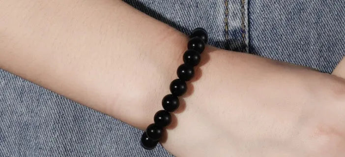 Close-up of a black agate bracelet with 8mm geometric beads on a black elastic cord.