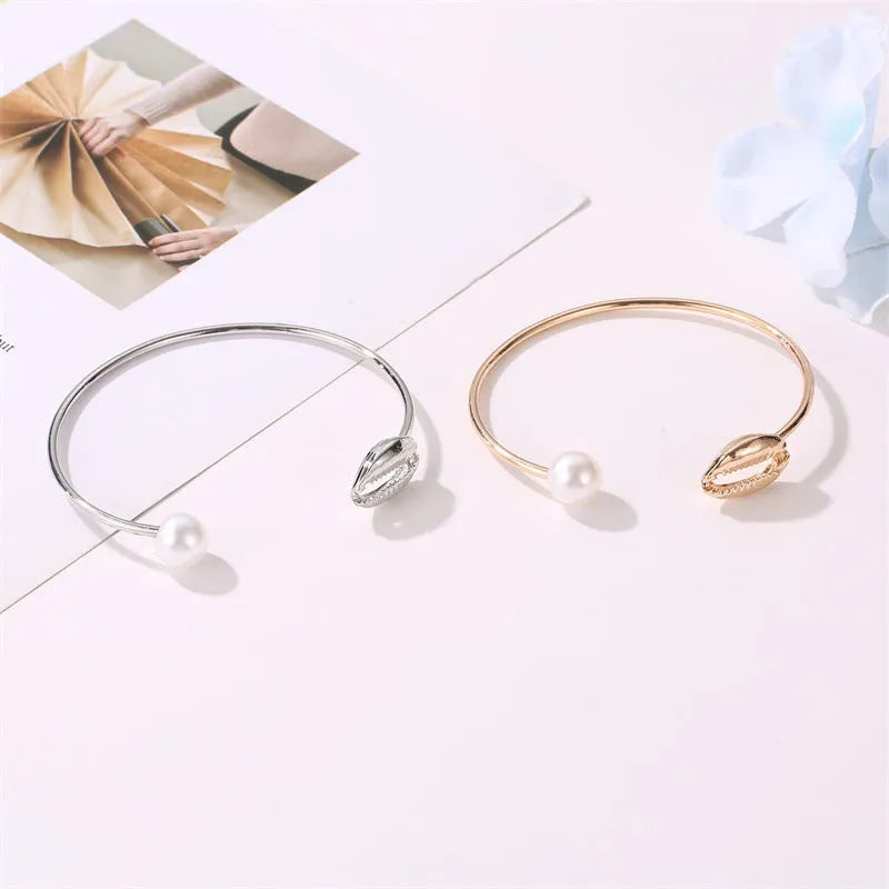 Alloy opening bracelet with pearl and shell decoration in gold finish on white background