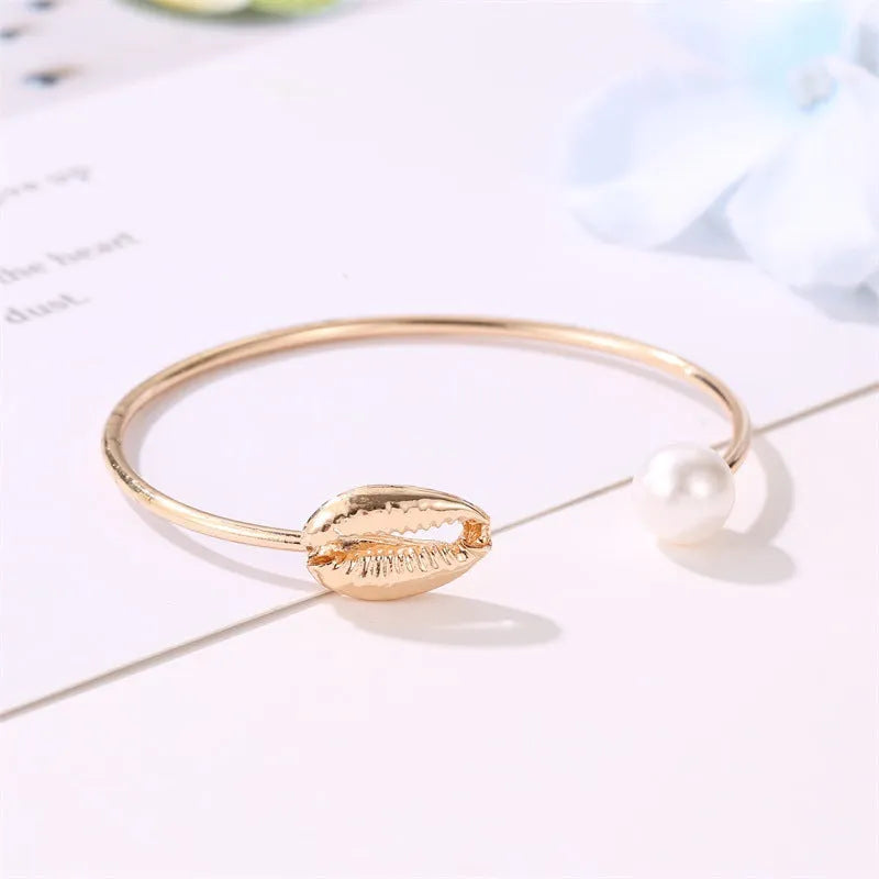 Alloy opening bracelet with pearl and shell decoration in gold finish on white background