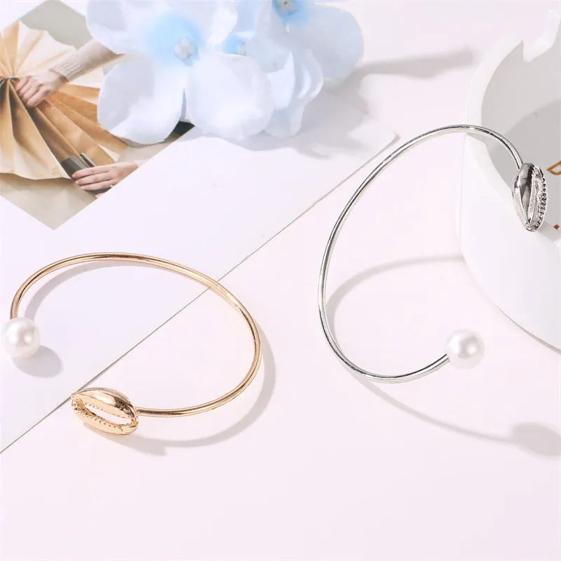Alloy opening bracelet with pearl and shell decoration in gold finish on white background