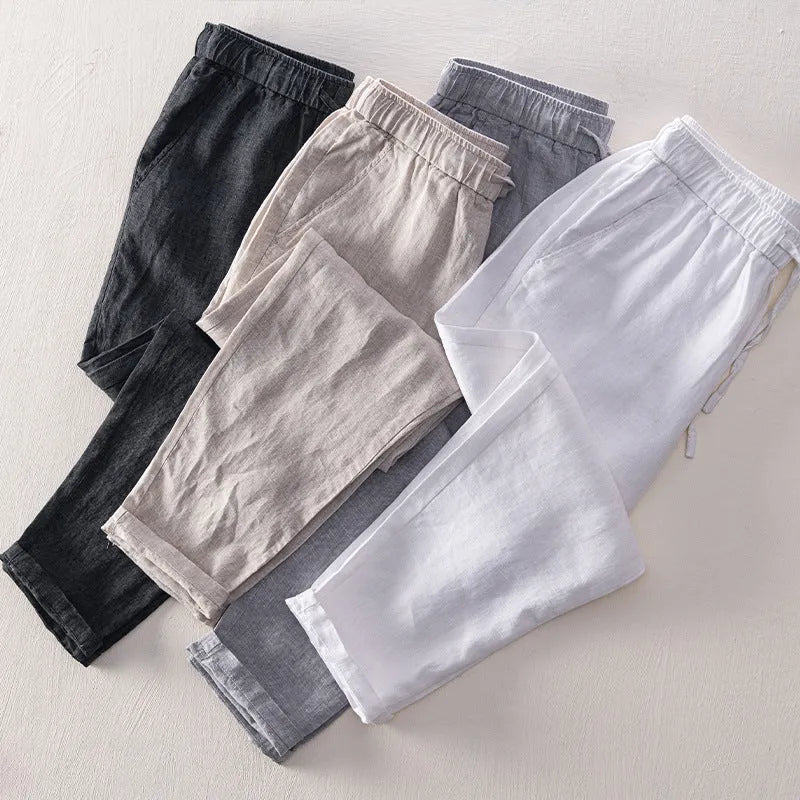 Men's straight-leg linen trousers in light grey, laid flat to show the mid-waist and tailored cut.