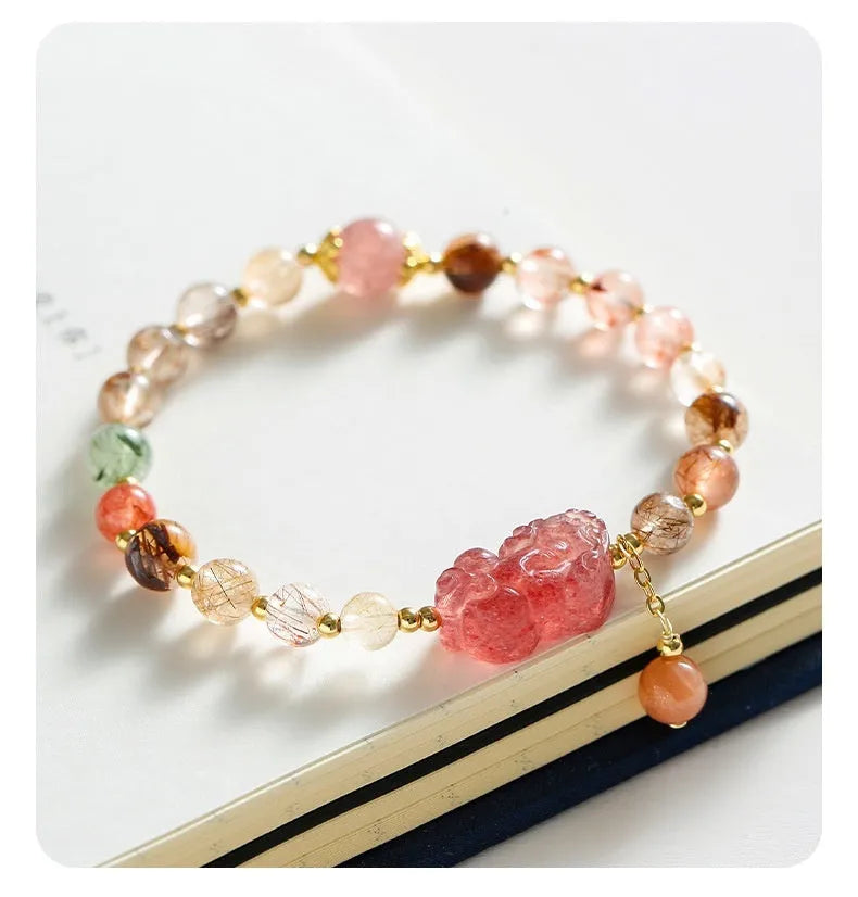 Copper women's bracelet with a pink Strawberry Quartz crystal and a gold-toned Pixiu charm, alongside smaller crystal beads.