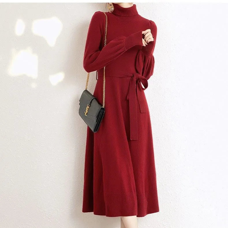 A woman wearing a rose red turtleneck long sleeve knitted dress with an elastic waist and a loose mid-length skirt.