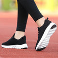 Women's black and pink running shoes showing fly weave upper texture and rubber outsole.