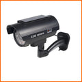 Black plastic gun-shaped dummy security camera with solar panel and red LED light indicator