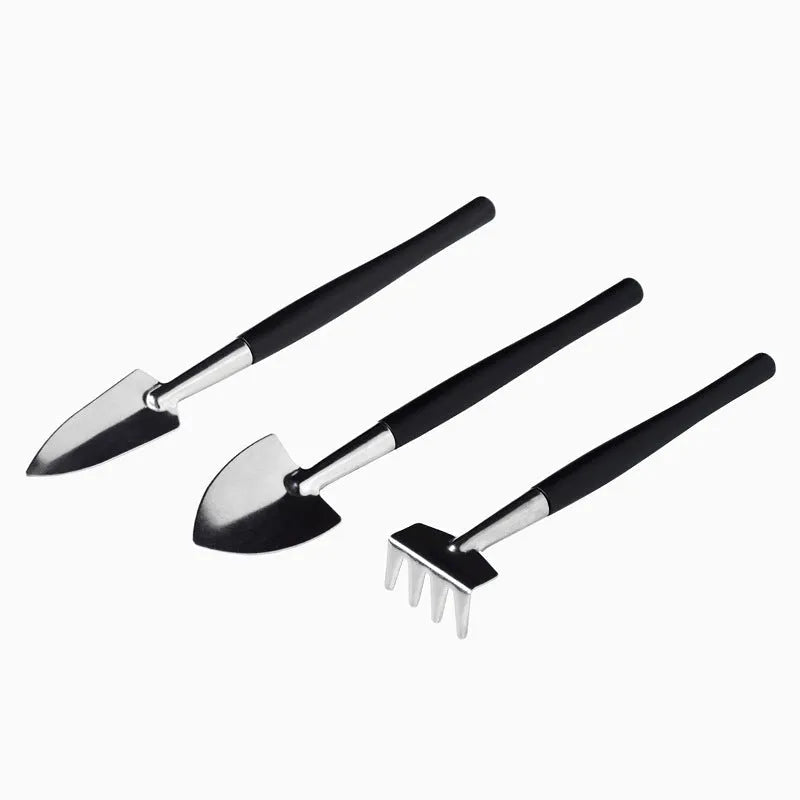 Black succulent garden tools set with shovel, tweezers, scissors, watering bottle and a square grey cushion.