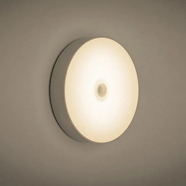 Small round white LED night light with motion sensor and USB charging cable on a table.