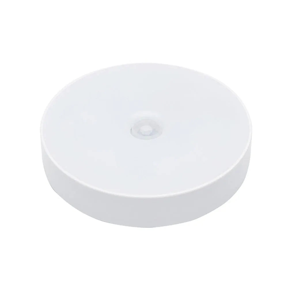 Small round white LED night light with motion sensor and USB charging cable on a table.