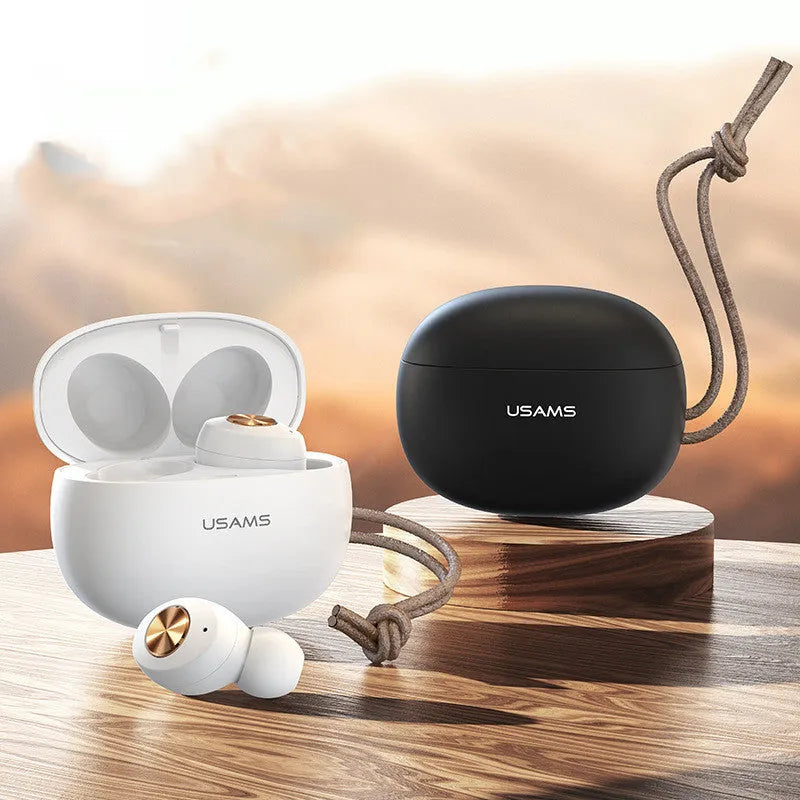 Wireless black TWS earbuds next to their small white charging case on a table.