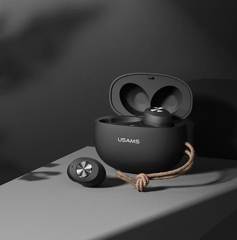 Wireless black TWS earbuds next to their small white charging case on a table.