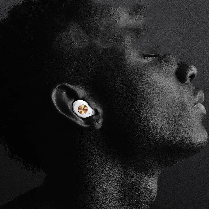 Wireless black TWS earbuds next to their small white charging case on a table.
