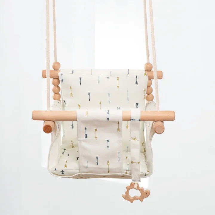 Natural beige cotton canvas baby swing chair with wooden seat and colourful tassel pendant, hanging indoors.