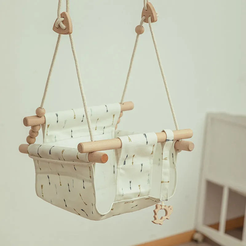 Natural beige cotton canvas baby swing chair with wooden seat and colourful tassel pendant, hanging indoors.