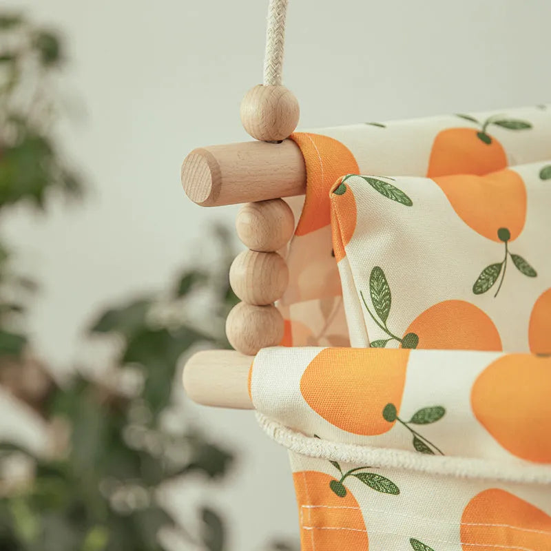 Natural beige cotton canvas baby swing chair with wooden seat and colourful tassel pendant, hanging indoors.