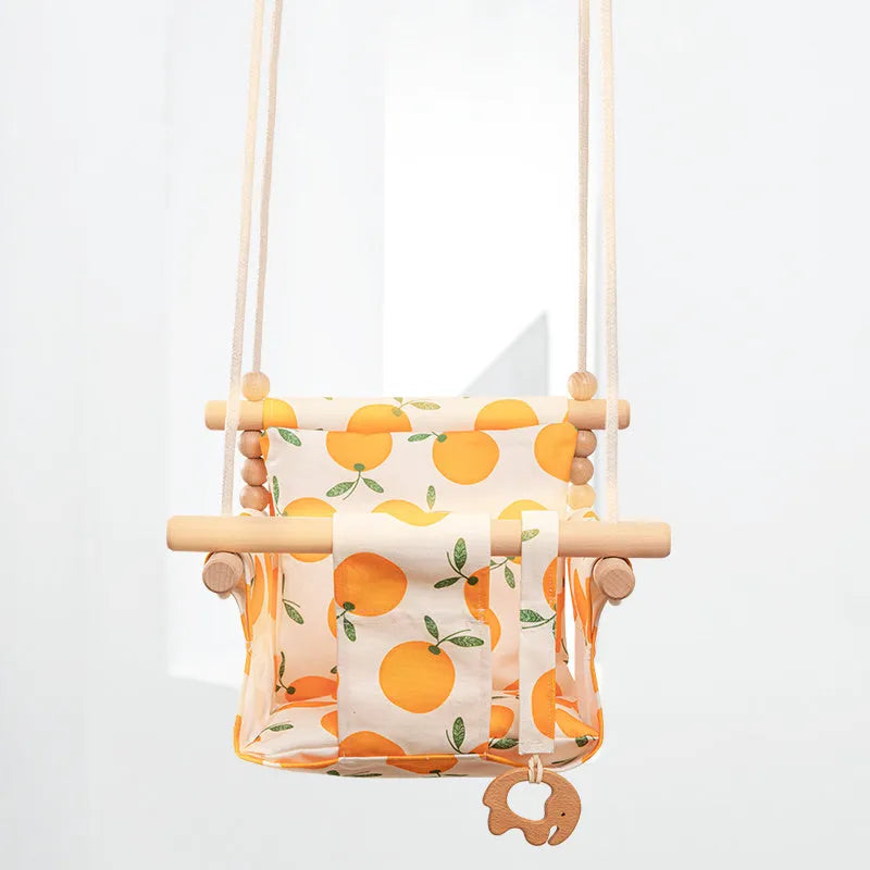 Natural beige cotton canvas baby swing chair with wooden seat and colourful tassel pendant, hanging indoors.