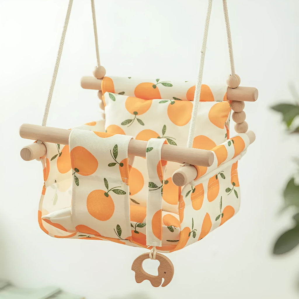 Natural beige cotton canvas baby swing chair with wooden seat and colourful tassel pendant, hanging indoors.