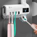 Black and white wall-mounted UV toothbrush steriliser with automatic toothpaste squeezer, showing solar panel and sensor.