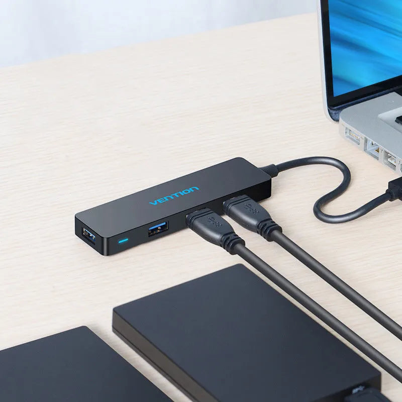 Black four-port USB 3.0 hub splitter with a short connected cable on a desktop.