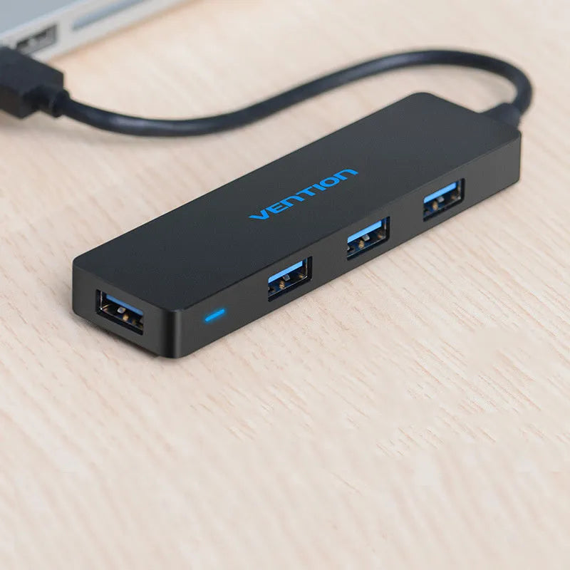 Black four-port USB 3.0 hub splitter with a short connected cable on a desktop.