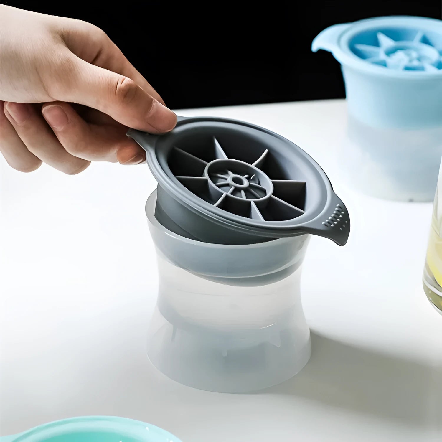 Flexible silicone ice tray producing large ice spheres, hockey puck shapes, and pentagon ice on a kitchen counter.