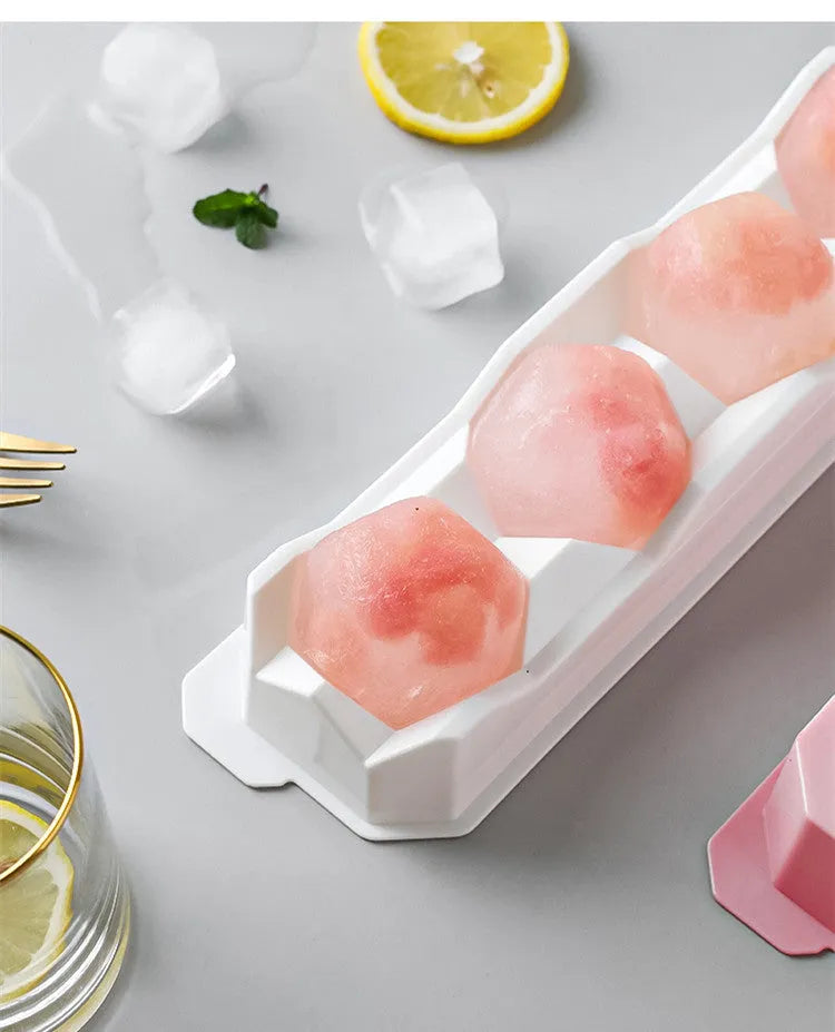 Flexible silicone ice tray producing large ice spheres, hockey puck shapes, and pentagon ice on a kitchen counter.