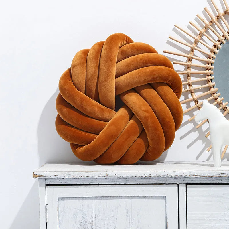 Square Nordic decorative cushion in caramel colour with a knotted ball design on a grey sofa.