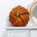 Square Nordic decorative cushion in caramel colour with a knotted ball design on a grey sofa.