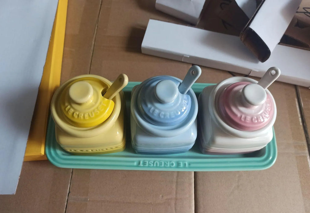 Three cool-coloured ceramic seasoning pots with a matching spoon on a kitchen counter