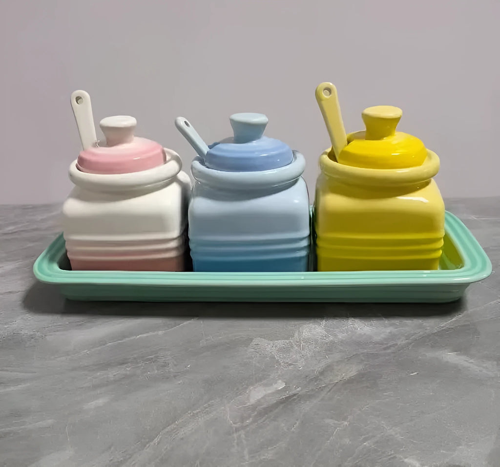 Three cool-coloured ceramic seasoning pots with a matching spoon on a kitchen counter