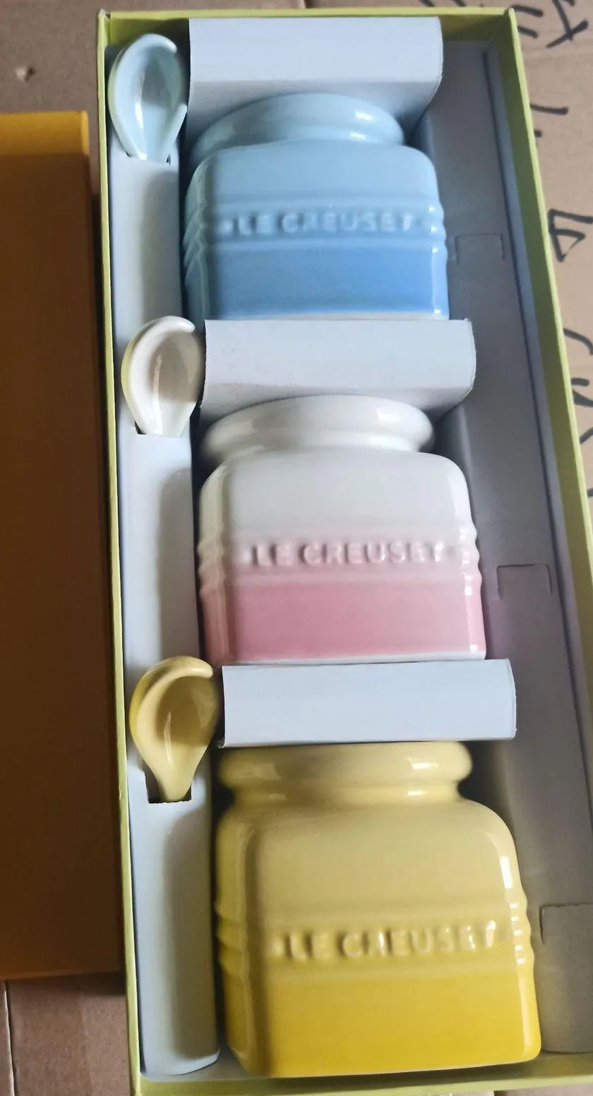 Three cool-coloured ceramic seasoning pots with a matching spoon on a kitchen counter